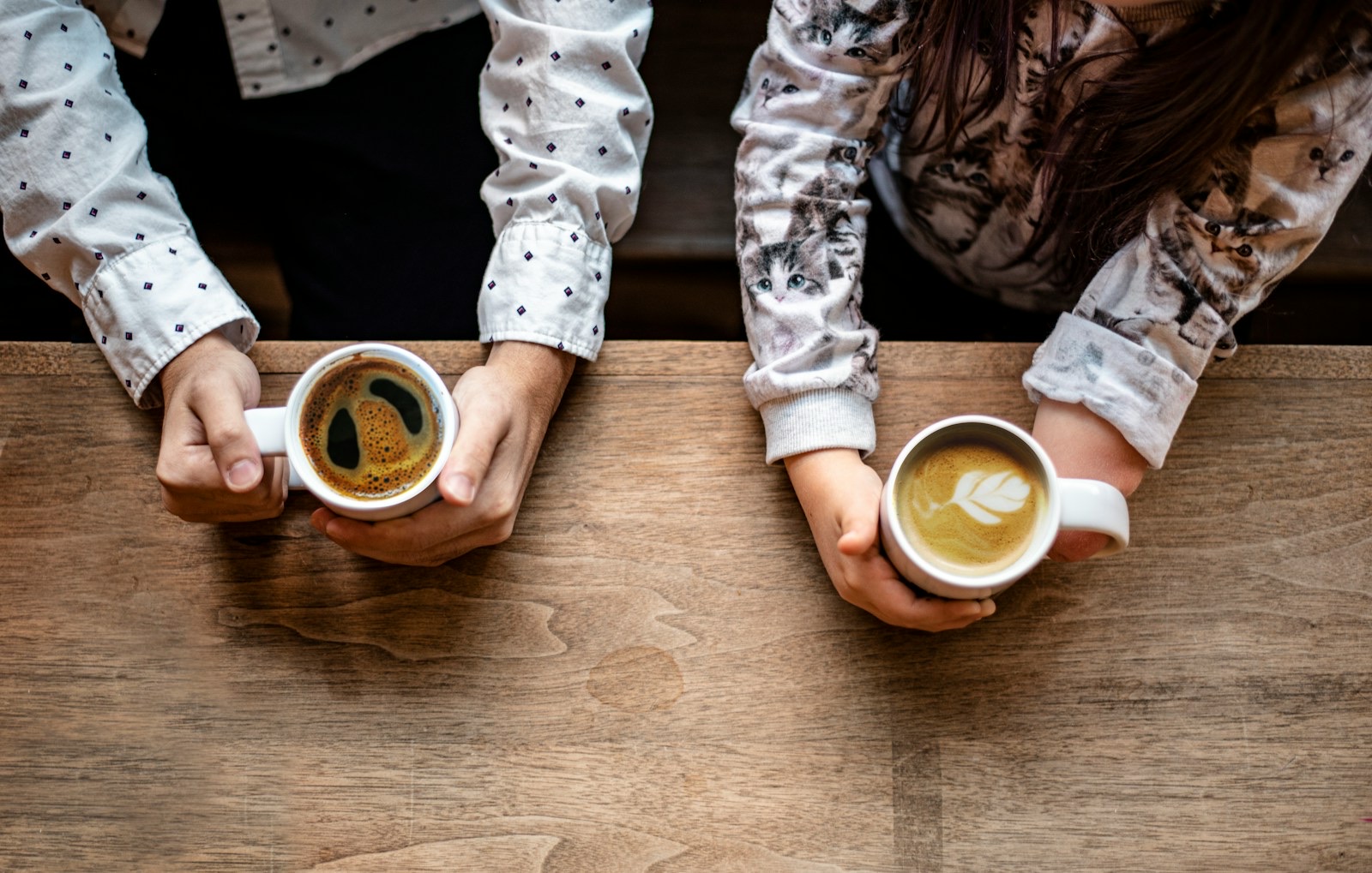 Two people holding cups of coffee across a wooden table