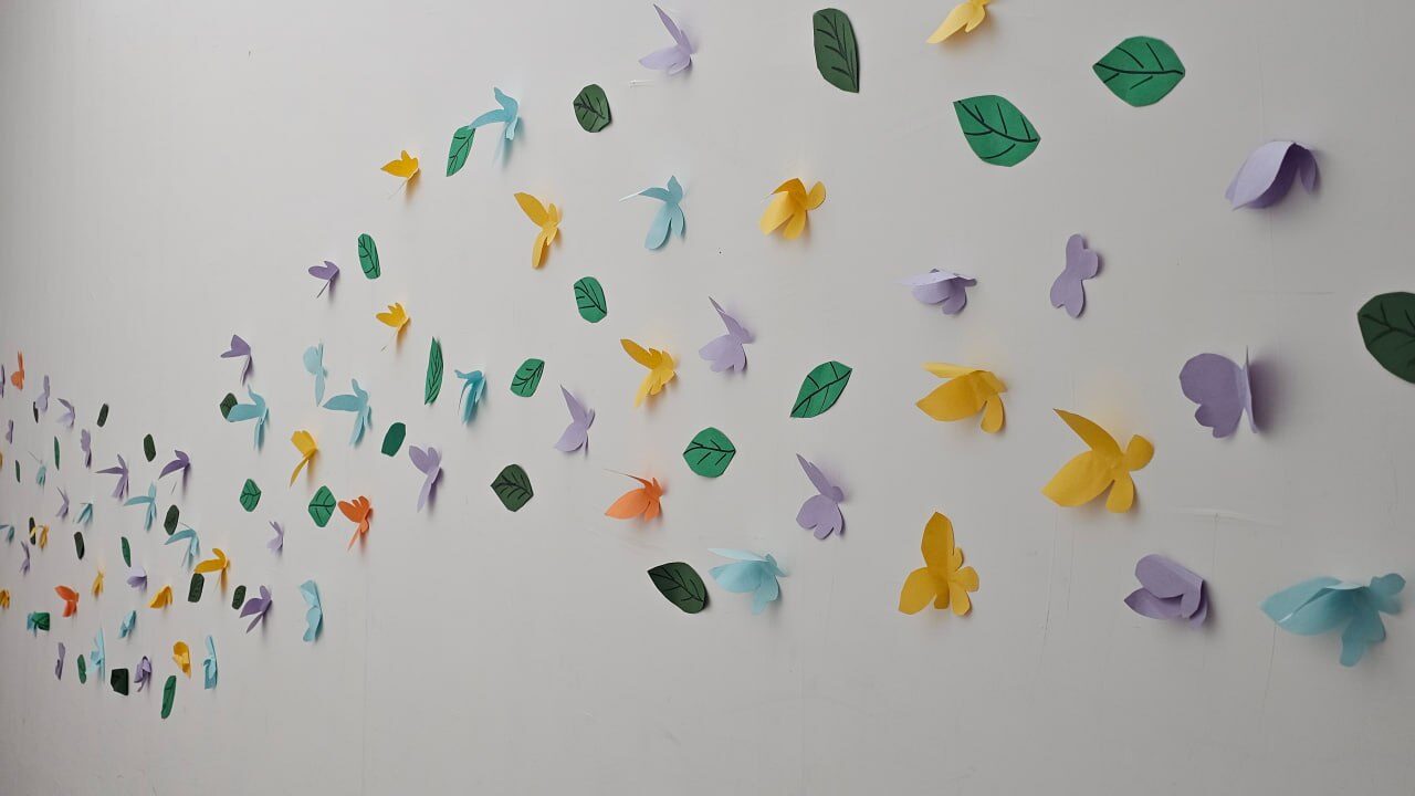 Paper butterflies and leaves flying across a wall