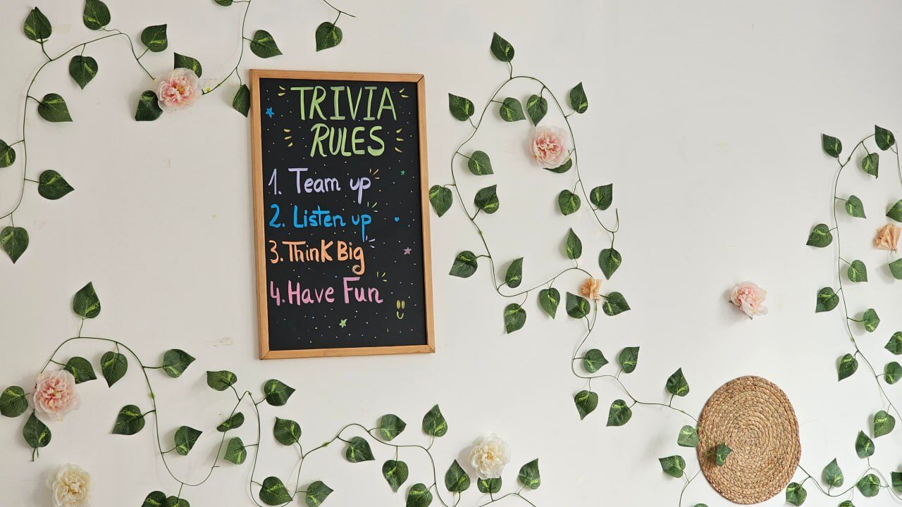 A trivia rules board on a wall of vines: team up, listen up, think big, have fun